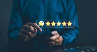 Müşteri Teftişi Memnuniyet Geribildirim Anketi Kavramı. Bir kişi beş yıldızlı bir not vermek için akıllı telefon kullanır, gülen yüz ikonu ile, müşteri memnuniyetini sembolize eder ve olumlu eleştiri.