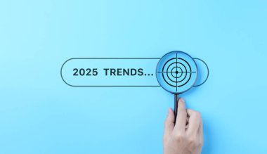 Trends 2025 year concept. Hand holding magnifying glass with 2025 trend searching bar for optimization 2025 business marketing trends and business plan in new year. Find information and new ideas. clipart