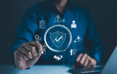 İş Güvenliği ve Uyum Konsepti. İş adamı elinde simgelerle büyüteç tutuyor iş güvenliği, uyum, risk yönetimi ve operasyonel verimlilik, güvenlik standartlarının önemini vurgulayarak.
