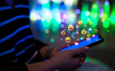 Sosyal medya teknolojisi konsepti. Ekranda yüzen çeşitli renkli emojili akıllı telefon kullanan bir kadın sosyal medya etkileşimini ve dijital iletişimi sembolize ediyor. Online pazarlama,