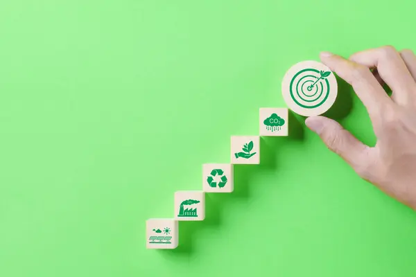 Yeşil Enerji ve Sürdürülebilir Konsept. Elinizde bir tahta blok, yeşil enerjili ve sürdürülebilirlik simgeleriyle yeşil arka planda hedef tahtası var. Karbon ayak izi, küresel ısınma, net sıfır,