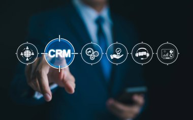 Müşteri Yönetimi için CRM Yazılımı. İş adamı, müşteri ilişkileri yönetimi, veri analizi ve müşteri desteği için dijital araçlar gösteren sanal bir CRM simgesine dokunur. Müşteri hizmetleri,