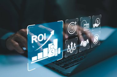 ROI ve İş Stratejisi Konseptleri analiz ediliyor. ROI 'yi, finansal stratejileri, yatırımları ve verimliliği temsil eden çeşitli dijital simgelerle bir dizüstü bilgisayarda çalışan bir işadamı. pazarlama planı,
