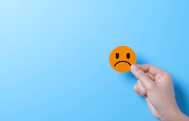 Sad Face Emoji Representing Negative Emotion. A hand holding sad face emoji, symbolizing negative emotions, dissatisfaction, and an unhappy customer experience. emotional or feedback related concepts. clipart