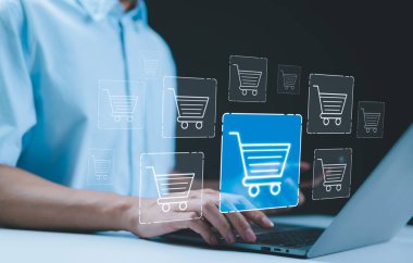 E-ticaret ve online alışveriş kavramları. Ekommersi ve çevrimiçi perakendeciyi temsil eden dijital alışveriş arabası simgelerine sahip bir dizüstü bilgisayar kullanan biri. İnternet alışverişi ve iş alışverişi olanağı.