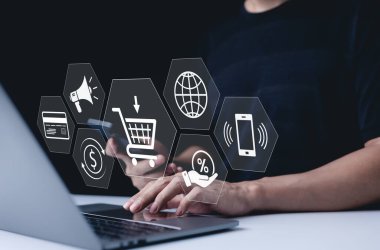 E-ticaret ve çevrimiçi alışveriş konsepti. E-ticaret, çevrimiçi alışveriş ve ödeme seçeneklerini temsil eden dijital simgelere sahip bir dizüstü bilgisayar kullanan bir kişi, İnternet tabanlı perakende satışlarının kolaylığını vurguluyor.