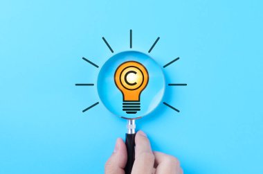 Fikir Eserleri ve Telif Hakları Koruma Konsepti. Telif hakkı sembolü, fikri, yeniliği, fikri mülkiyeti ve yaratıcı endüstrilerde patent korumasına sahip ampul simgesine büyüteç konması.