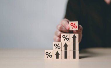Faiz Oranı ve Büyüme Kavramı. Yüzde sembolleri olan tahta bloklar ve kademeli olarak istiflenmiş oklar, faiz oranlarını, finansal büyümeyi ve ekonomideki kar paylarını temsil ediyor..