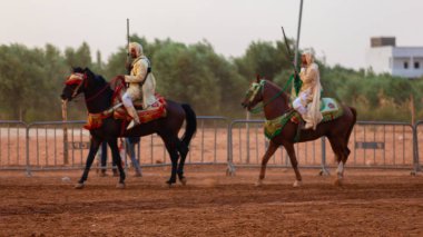 Essaouira, Fas - 13 Ağustos 2023: Biniciler geleneksel Fas kıyafeti ve şövalyelerin aksesuarları içinde Arapça Tbourida adlı geleneksel bir giysi etkinliğine katılıyorlar