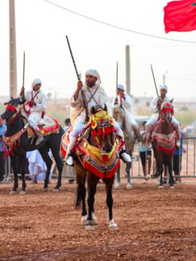 Essaouira, Fas - 13 Ağustos 2023: Biniciler geleneksel Fas kıyafeti ve şövalyelerin aksesuarları içinde Arapça Tbourida adlı geleneksel bir giysi etkinliğine katılıyorlar