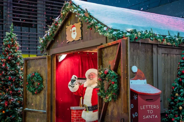 Noel Market 'te kar yağan bir gecede Noel Baba' yı sallamak etrafı süslenmiş ağaçlar, posta kutusu ve kış tatili süslemeleriyle çevrili, Lansdowne Park, Ottawa, Ontario, Kanada. Fotoğraf Aralık 2021 'de çekildi..