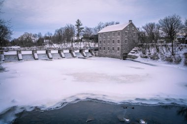Watsons Mill bir müze ve tarihi yer ve kış boyunca baraj, donmuş Rideau Nehri 'nde iki ördek, Manotick, Ottawa, Ontario, Kanada. Fotoğraf Şubat 2022 'de çekildi..