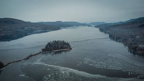 Aerial photo of icy Lake Tremblant in winter wedged between mountainous rides at the foot of Mont Tremblant mountain in the Laurentides region of Quebec, Canada. Photo taken by drone in December 2023.