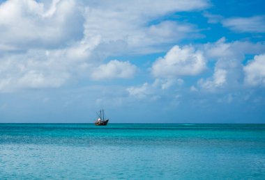 Karayip Denizi 'nin açık turkuaz sularında bir korsan gemisi tur teknesi. Ufuk ve gökyüzünün manzara fotoğrafı Palm Beach, Noord, Aruba, Hollanda adasından alınan güzel beyaz bulutlar Şubat 2024.