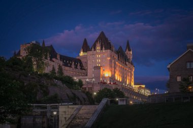 Night view of the iconic Fairmont Chateau Laurier hotel illuminated under twilight blue hour sky, dramatic purple clouds, above the historic Rideau Canal locks, Ottawa, Ontario, Canada August 2022 clipart