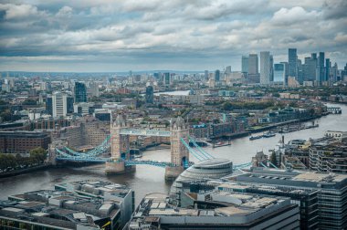 Thames Nehri 'ni kaplayan ve arka planda şehir silueti olan Londra Kulesi Köprüsü' nün geniş hava manzarası, bulutlu bir günde modern gökdelenlerle ikonik mimari tezat oluşturuyor.