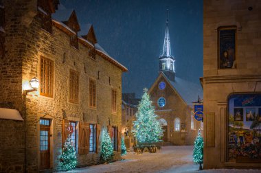 Quebec 'teki Place Royale' de büyülü karlı bir akşam, aydınlanmış Noel ağaçları ve Quebec City, Kanada, Aralık 2022 'de neşeli bir kış ortamı altında ikonik Notre-Dame-des-Victoires Kilisesi.