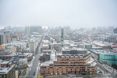 Montreal şehir merkezinin kış kar yağışı altında hava görüntüsü, karla kaplı binalar, sisli ve bulutlu siluet, kentsel kışın özünü yakalayan sahne, Quebec, Kanada Ocak 2025