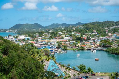 Castries, Saint Lucia 'nın canlı hava manzarası, renkli binalar, yemyeşil tepeler, tekneli sakin körfez, mavi gökyüzü altında tropikal manzara, mükemmel Karayip seyahati ve şehir manzarası Şubat 2025