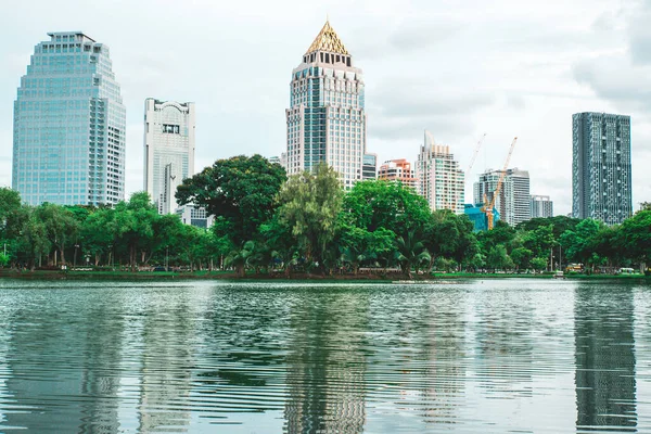 Cityscape of Lumpini Park with skyscrapers, lake and green trees during daytime. Downtown area in Silom district, Bangkok, Thailand.