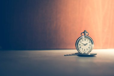 Tarafsız ahşap bir zemin üzerinde gölgeli bir atmosferde klasik cep saati, metin için boş alanı olan yumuşak mavi tonlarda görüntü