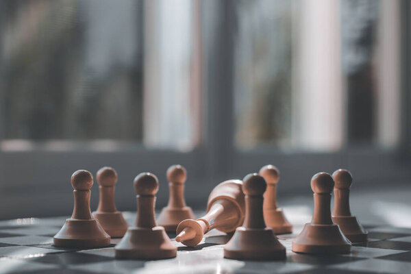 fallen white king surrounded by white pawns on a chessboard in a gloomy atmosphere. The fallen leader surrounded by his team. team members regret and mourn the loss of a leader.