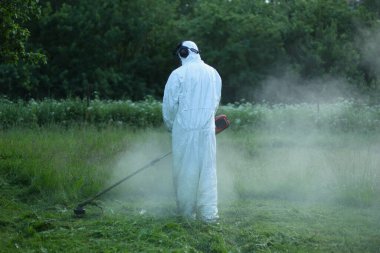 Bir adam çimleri budayarak buduyor. Beyaz koruyucu takım elbiseli bir erkek..