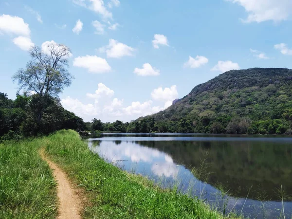 stock image Tranquil Sri Lankan Village: A Beautiful Lake View with Mountains and a Narrow Path Surrounded by Green Grass