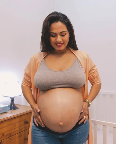 妊娠中ラティーナ女性見て彼女の腹隣彼女の赤ちゃんの白いベビーベッド — ストック写真