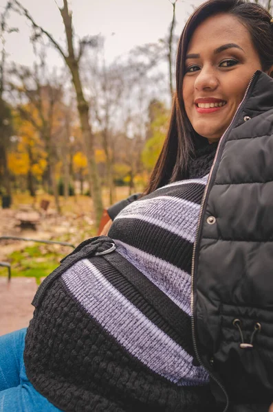 秋には黒い服を着た妊婦が公園の椅子に座っています — ストック写真