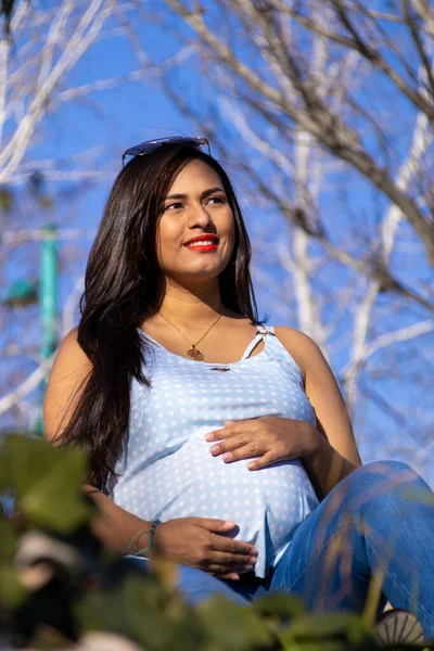 Беременная Молодая Латиноамериканка Сидящая Траве Улыбающаяся Смотрящая Горизонт Голубой Одежде — стоковое фото