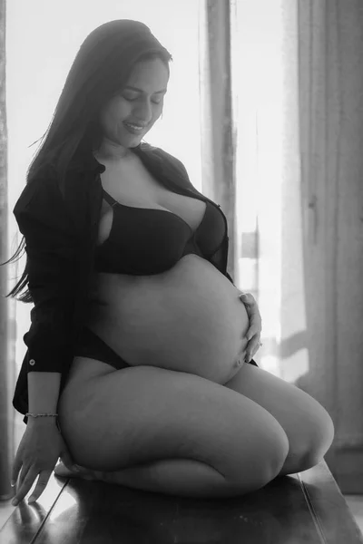 Młoda Latynoska Ciąży Kolanach Dotykająca Brzucha Ubrana Czarną Bieliznę Oknem — Zdjęcie stockowe