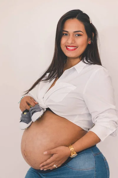 怀孕的年轻拉丁女子一边笑一边抱着小鞋 — 图库照片