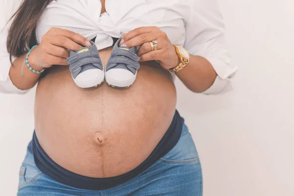 妊娠中の女性身に着けています小さな白い靴上の彼女の腹とCopyspace — ストック写真