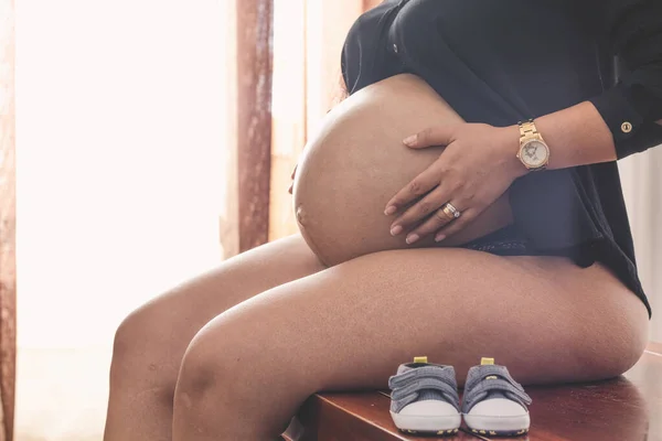 若いです妊娠中の女性座っています彼女の腹に彼女の手 黒ブラウスと小さな灰色の靴隣に彼女 — ストック写真