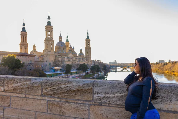 stock image Pregnant young woman looking at the Pilar Cathedral from the stone bridge in Zaragoza, Spain.