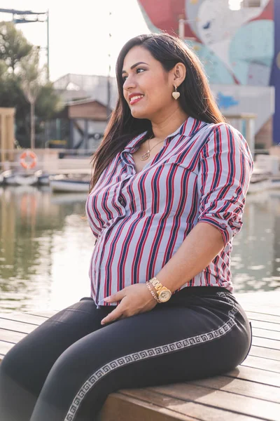 妊娠中のラティーナの女性は桟橋に座って 笑顔と地平線を見て — ストック写真