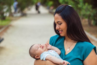 Genç anne gülümsüyor ve parkta bebeğine bakıyor..