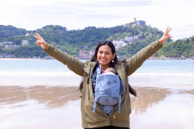 Latin anne bebeğini mavi bir bebek arabasında taşıyor, kumsalda ve ilkbaharda kollarını açarak mutlu..