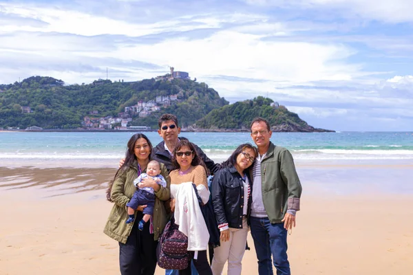 Latin family of five adults and a baby, smiling on the beach and in the springtime.