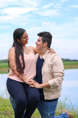 Latin çift birbirlerine bakıp göl kenarında gülümsüyorlar.