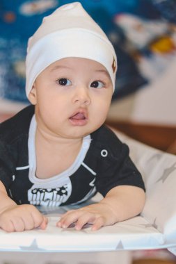 Siyah takım elbiseli, beyaz şapkalı, sırtüstü uzanmış, uyanmış ve Evren 'in arka planına sahip kameraya bakıyor.