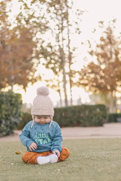 Güzel erkek bebek sonbaharda parkta oturmuş ayakkabılarına bakıyor.