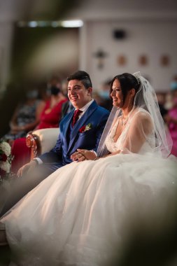 Neşe saçan bir çift, zarif bir ortamda sevdikleriyle el ele oturur. Düğün kıyafetleri içinde, heyecan ve duyguyla dolu anlamlı bir anı paylaşıyorlar..