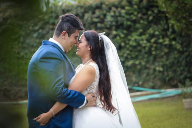 Etrafı yeşilliklerle çevrili bir çift birbirine yakın durur ve birbirlerine sevgiyle bakar. Sıcak güneş, özel günlerinin neşe ve heyecanını vurgular..