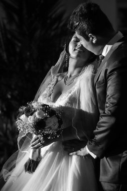 Neşeli çift, birbirlerine bakıp, yakından bakıyorlar. Gelin, narin bir elbise içinde, bir buket tutarken damat nazikçe belini kucaklıyor.