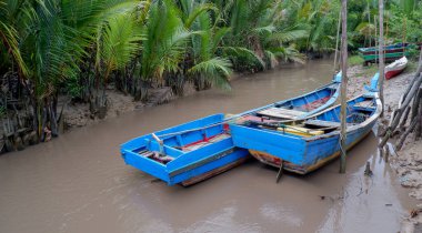 Endonezya 'da çamurlu bir nehrin kıyısına demirlenmiş birkaç mavi balıkçı teknesi.