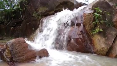 Büyük kayaların tepesinden akan şelalenin yanındaki kayaların manzarası.