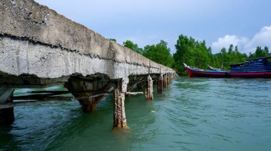 Kırık sütunlarla beton iskele, yüksek dalgalar ve tekne, arka planda Avicennia Marina Ormanı, Belo Laut Köyü, gündüz vakti