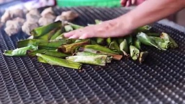 Bir kadının eli şöminede özel yemek pişiriyor. (Otak-otak)